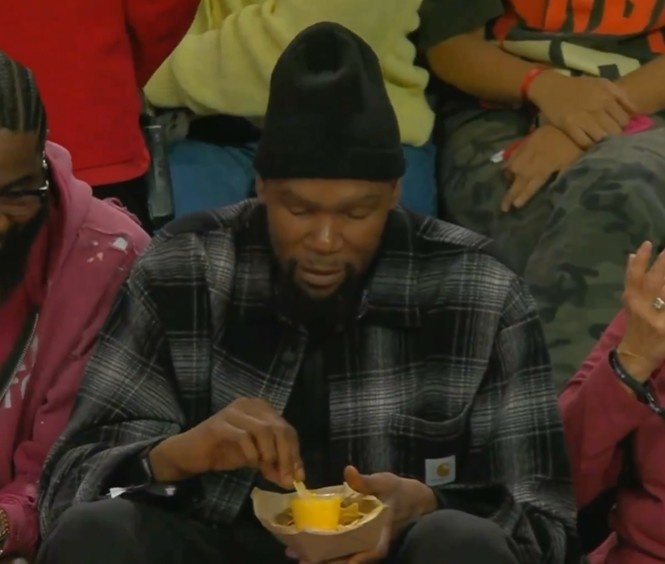 杜兰特场边观战WNBA 头戴黑帽薯片蘸酱